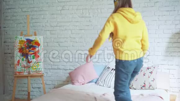 可爱的女孩正在家里的床上跳舞一边用耳机听音乐一边跳一边举手现代的视频的预览图