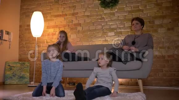 白种人母亲的家庭肖像三个女儿坐在沙发上在平静的家庭氛围中看电影视频的预览图