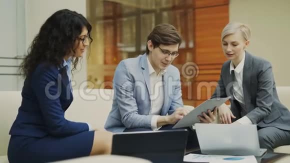 戴眼镜的商人和坐在沙发上开会的女商人谈未来的合同视频的预览图