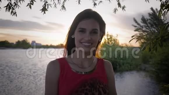 黄昏时分在池塘背景下一位迷人的微笑年轻女子的肖像视频的预览图