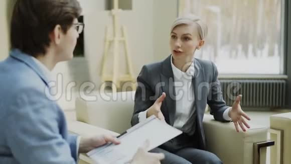 女商人与坐在扶手椅上的男商业伙伴谈论和嘲弄公司财务信息视频的预览图