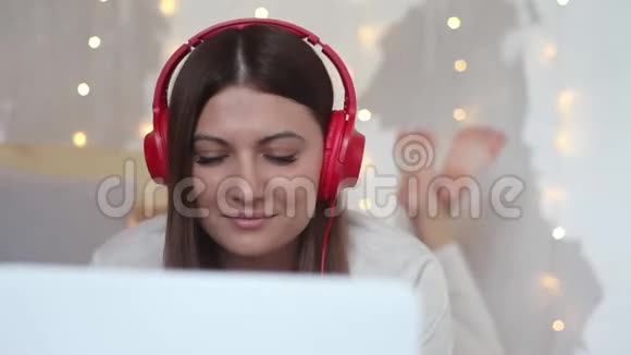 一个漂亮的女孩躺在床上用移动电脑用耳机听音乐高清特写视频的预览图