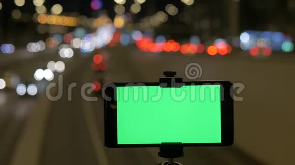 一部带有绿色屏幕的智能手机被固定在路上在汽车美丽的红绿灯的背景下视频的预览图