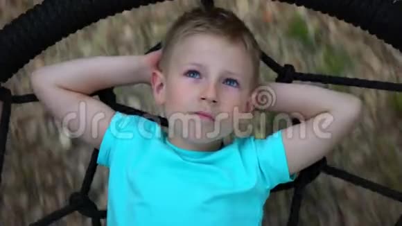 蓝眼睛的五岁男孩躺在一个圆秋千上双手仰起头抬头望着天空视频的预览图