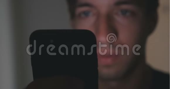 在家里的飞镖室用智能手机关闭年轻人他脸上的智能手机反射视频的预览图