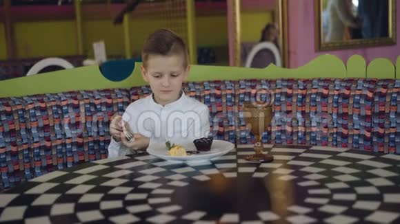 英俊的微笑男孩开始在咖啡馆里吃美味的甜点4K视频的预览图