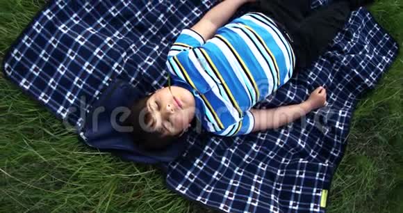 一个嘴里长着一片草的男孩闭着眼睛在绿色草坪上的地毯上做梦视频的预览图