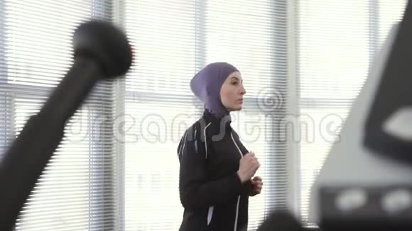 戴着头巾的女运动员在跑步模拟器上慢动作视频的预览图
