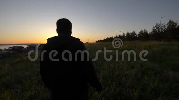 年轻的非洲男人在美丽的夕阳下漫步在夏夜的田野视频的预览图