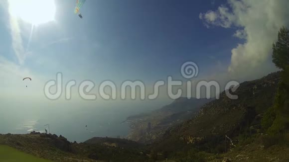 滑翔伞在阳光明媚的日子飞过山丘海边城市在脚下极限运动视频的预览图