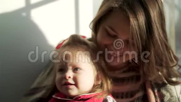 美丽的女婴可爱的胖乎乎的脸颊在母亲的怀里微笑可爱的孩子和她妈妈靠在窗户上视频的预览图