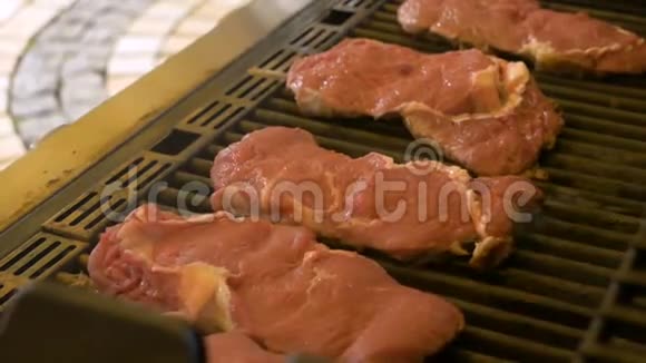 大的生肉牛排在煤气烤架的格栅上烤盘子里冒出一小股烟专业人士烧烤视频的预览图