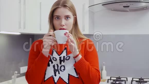 穿红色毛衣的漂亮姑娘在厨房喝茶视频的预览图