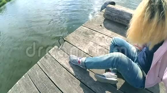 穿着蓝色牛仔裤的金发女孩坐在一个古老的木墩边上视频的预览图