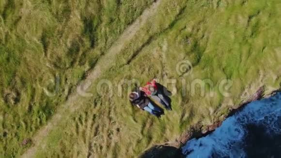 两个女孩躺在爱尔兰海岸悬崖的草地上从上面看到无人驾驶飞机视频的预览图