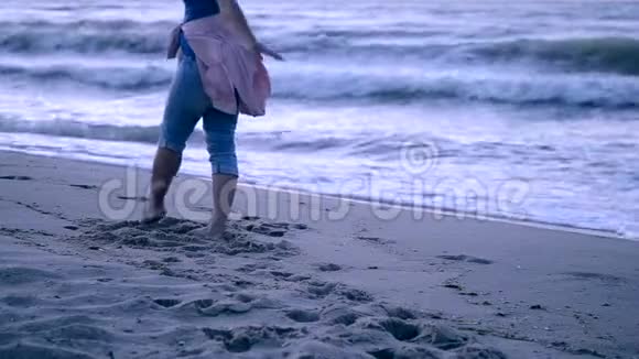 一个穿着蓝色牛仔裤和系在腰带上的粉红色夹克的女孩来到大海视频的预览图