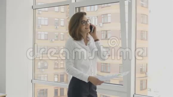 办公室工作人员戴眼镜的女商人在办公室里看文件打电话视频的预览图