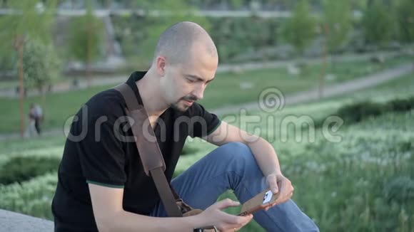 一个年轻人拿着电话坐在公园里写短信视频的预览图