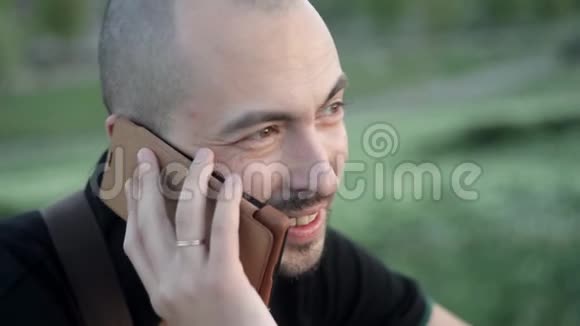 微笑的年轻人坐在公园里手里拿着一个绿色植物的背景下打着电话视频的预览图