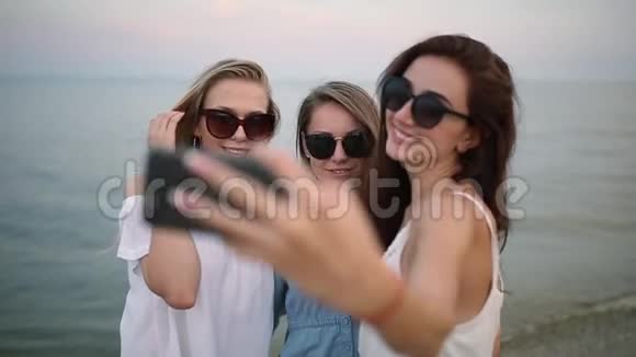 三个年轻女人在海滩上自拍海景朋友们在微笑地看着相机穿着衣服的女孩视频的预览图