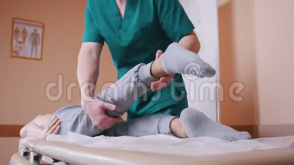 手动治疗师按摩躺在按摩台上的年轻女性伸展和弯曲她的髋关节和下背部视频的预览图