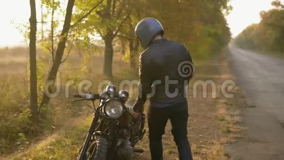 戴着头盔和皮夹克的年轻人来到他的自行车前发动引擎同时站在路边穿着一件视频的预览图