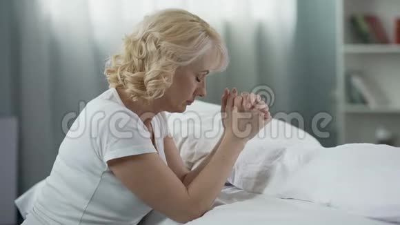 老年女性坐在床旁的地板上祈祷宗教信仰视频的预览图