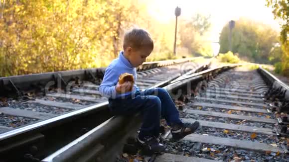 孤独的男孩坐在铁轨上危险的游戏和娱乐活动秋天温暖的一天视频的预览图