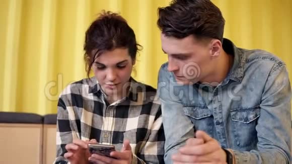 一对夫妇坐着聊着什么年轻迷人的女孩在她的智能手机上给她的男朋友看一些东西视频的预览图