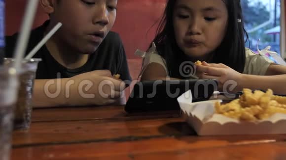 快乐的亚洲孩子在手机上观看享受吃土豆火兄弟姐妹在餐厅的慢动作视频的预览图