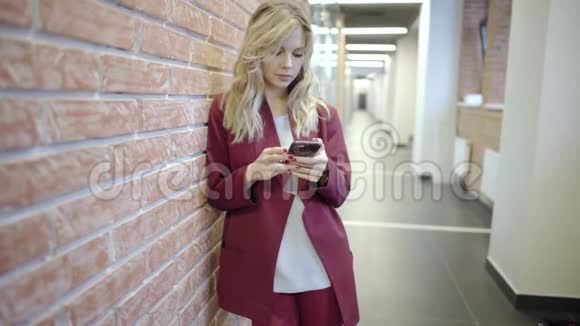 漂亮的金发女商人带着智能手机在办公室大厅上网视频的预览图