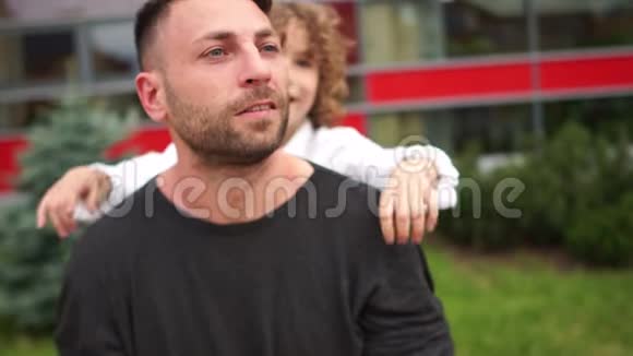 一个漂亮的卷发男孩从背后拥抱他的父亲父亲节幸福的家庭视频的预览图