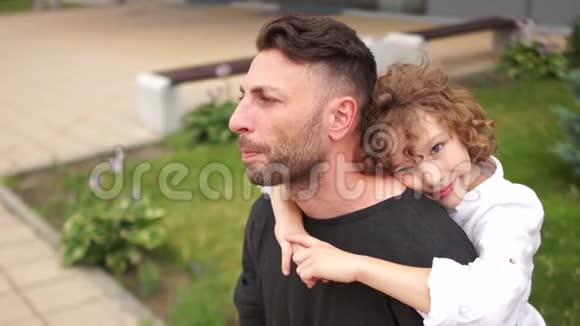 一个脸严肃的年轻人坐在长凳上他被一个卷发男孩拥抱父子父亲节视频的预览图