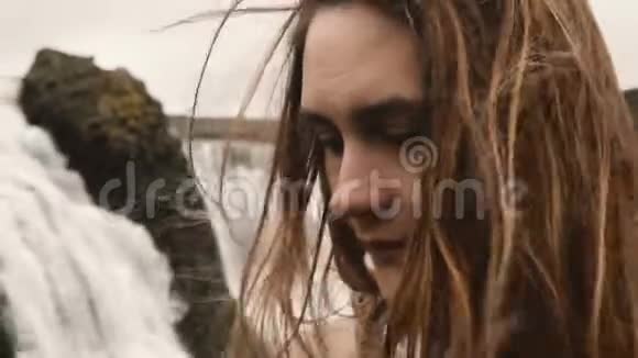 冰岛瀑布附近站着的年轻美丽悲伤的女人的肖像环顾四周头发随风飘扬视频的预览图