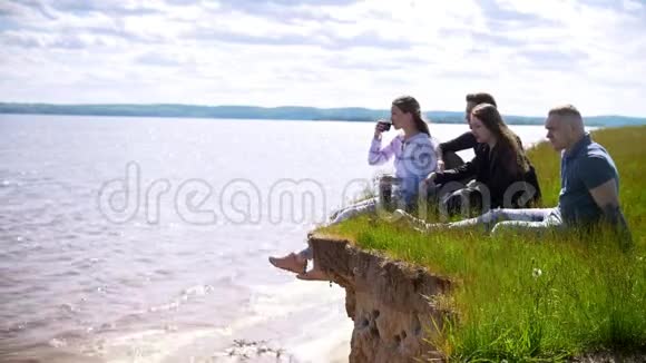 快乐的朋友坐在河边的山上享受娱乐和喝茶视频的预览图