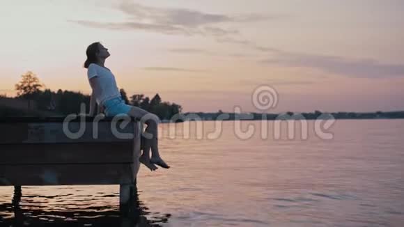 年轻苗条的女人正坐在水面之上在夏日夕阳的照耀下放松视频的预览图
