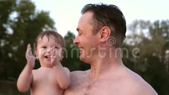 小湿澡的孩子拍拍手笑着坐在爸爸的怀抱里视频的预览图