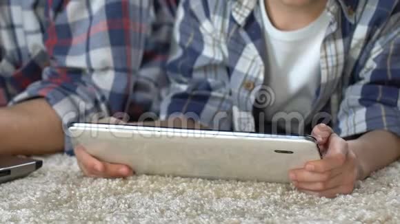 父亲在笔记本电脑上工作儿子在他附近的地板上玩平板电脑游戏视频的预览图