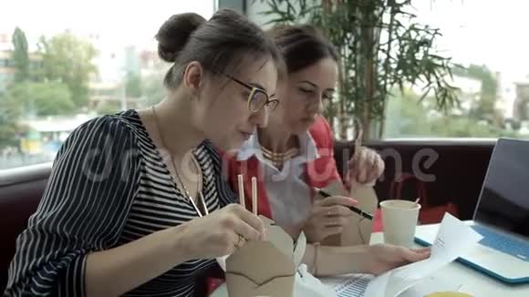两个年轻的商务女孩午餐吃中国面条喝咖啡考虑到生意的发展视频的预览图