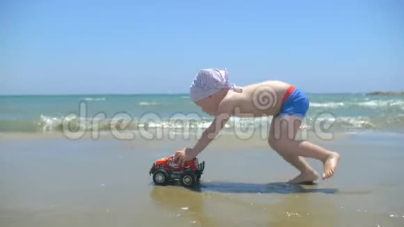 可爱的男孩在海滩上玩玩具车儿童推手玩具卡车视频的预览图