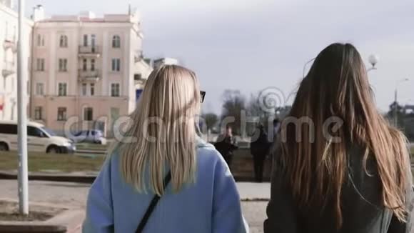 慢动作两个女孩一起走在街上年轻女士穿着时尚的衣服留着漂亮的长发后景视频的预览图