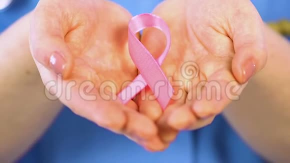 女人在手心轻轻地握着粉红色的丝带支持患有乳腺癌的女人视频的预览图