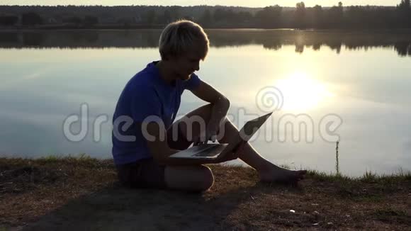 blondman在slomo的一个湖畔用他的笔记本电脑工作视频的预览图