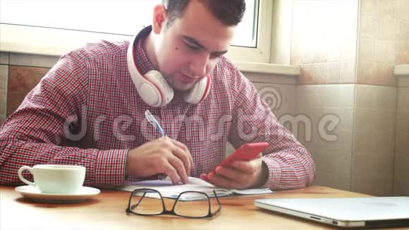 年轻的商人坐在桌边喝咖啡做工作写在一本书里忙碌的人写作业股票视频的预览图