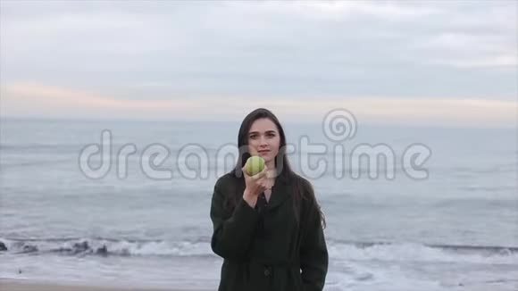 一个穿着深绿色外套的漂亮女孩海边有一个绿苹果视频的预览图