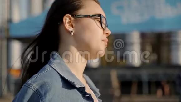 戴眼镜的漂亮年轻女孩穿过城市环顾四周戴眼镜的女孩的肖像视频的预览图
