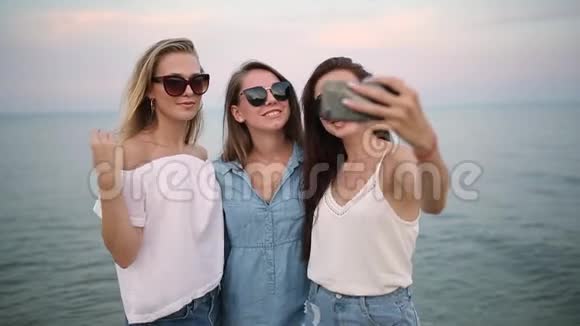 三个年轻女人在海滩上自拍海景朋友们在微笑地看着相机穿着衣服的女孩视频的预览图