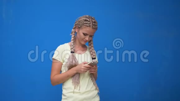 欢快可爱的年轻女学生留着辫子扎着辫子留着发式用手机聊天的照片视频的预览图