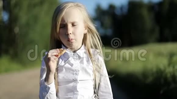 饥饿的学校女孩穿着白色衬衫和黑色裙子走在沙地路上穿过田野吃了一块饼干视频的预览图