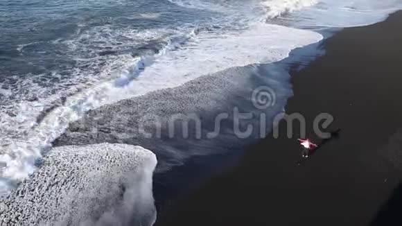一个年轻的女人沿着海滩奔跑用手旋转和触摸水波浪在黑色的PLZH上滚动冰岛视频的预览图